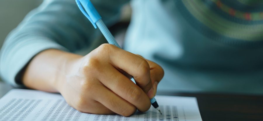 Close up of high school or university student holding a pen writing on answer sheet paper in the examination room. College students answering multiple choice questions test in the testing room in university.