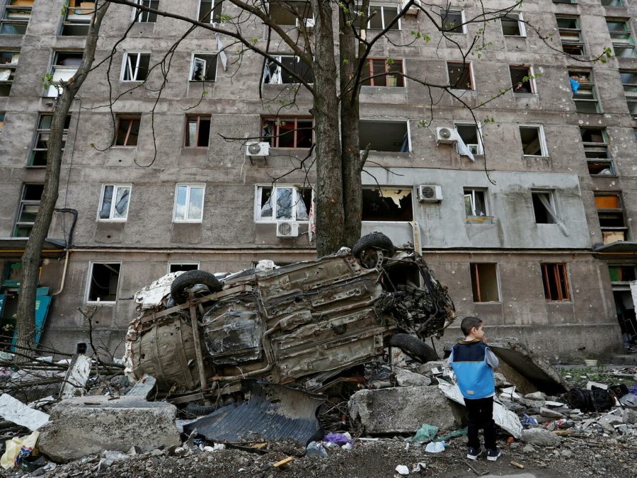 FILE PHOTO: A boy stands next to a wrecked vehicle in front of an apartment building damaged during Ukraine-Russia conflict in the southern port city of Mariupol, Ukraine April 24, 2022. REUTERS/Alexander Ermochenko/File Photo